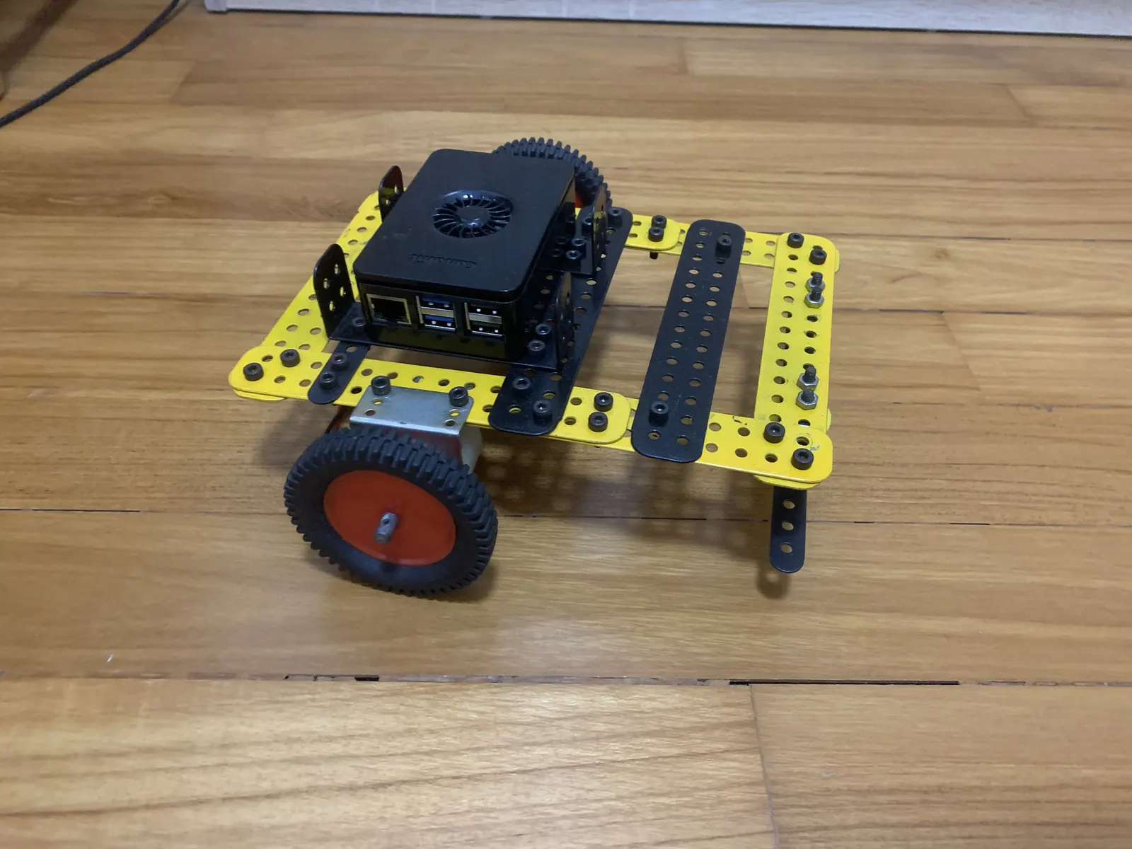 CANIS chassis prototype — a Raspberry Pi 5 in a black case mounted on a yellow and black metal chassis with drive wheels